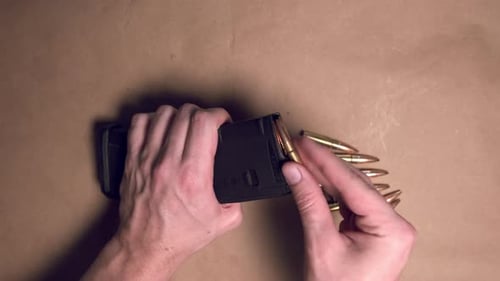 Close up shot of hands loading a rifle magazine with bullets. Top down shot