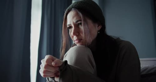 A Brunette Girl Leans on Her Knee and Sits on the Sofa Upset and Desperate