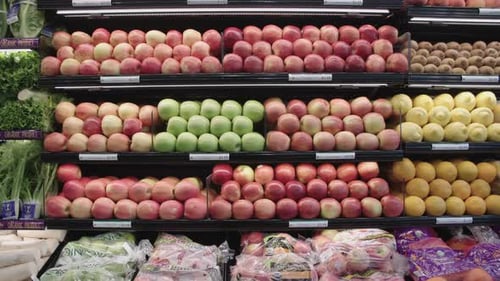 Various apples and citrus fruit on display shelves in the produce section at a grocery market.