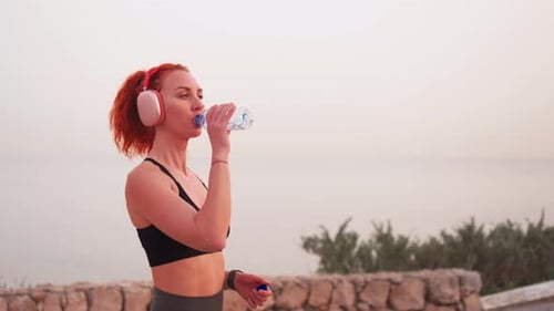 Smiling Sporty Woman Drinking Water From Bottle Against Sea