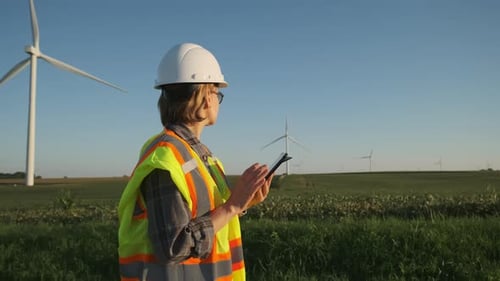 Eine Ingenieurin in einem Windpark mit einem Tablet in der Hand stellt die Windkraftanlage ein