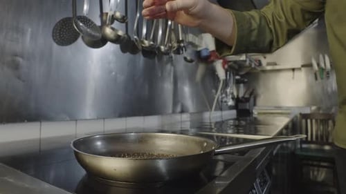Chef adds spices to oil in pan in kitchen