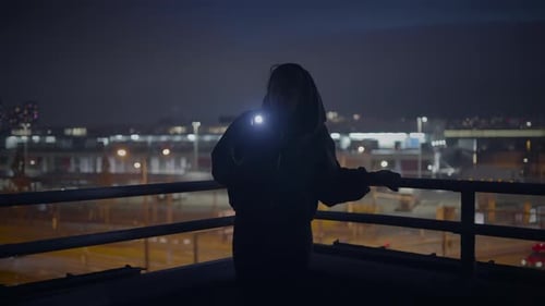 Mysterious Person with a Flashlight on a Rooftop Creating an Enigmatic City Atmosphere at Night