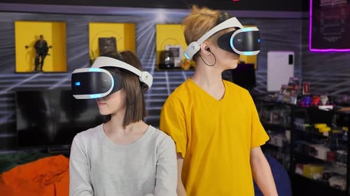 Friends with a Virtual Reality Headset in Glasses and Hand Motion Controllers in the Gaming Club