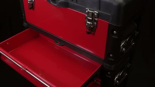 A close-up of a man opening shelves in a red metal tool cabinet at a service station