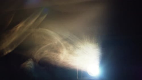 Smoke Stream Seeps Through Hole and Reflects in Light