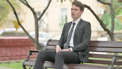 Man in Suit Coughing on a Park Bench