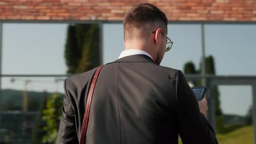 Portrait Businessman in Suit with Glasses Stand Near Modern Building Holding Smartphone in Hands