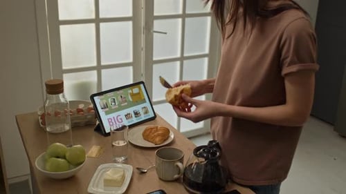 Woman Using Tablet and Eating Croissant at Breakfast