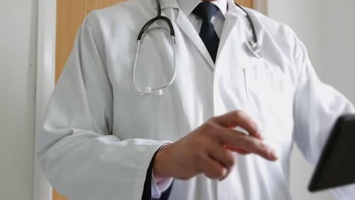 Close up of a doctor using a tablet computer in a hospital. The unrecognizable man is standing outsi