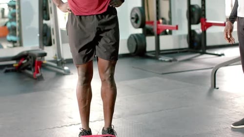 African American male trainee at gym looping band at feet performing knee raises for strength