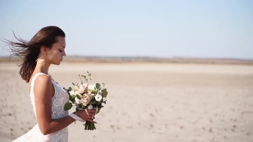 Romantic Bride with Delicate Wedding Bouquet at Desert Landscape Hair of Pretty Woman Blowing in a