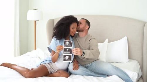 Expecting Couple Holding Ultrasound Image in Bedroom