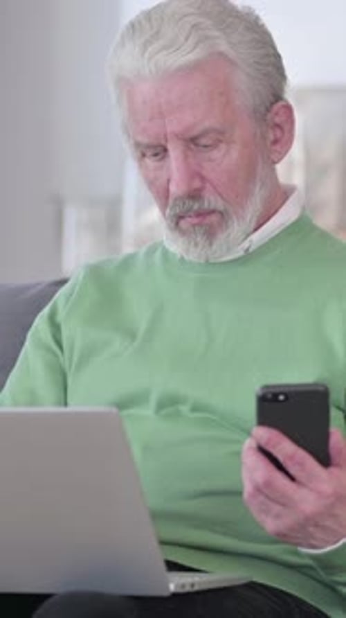 Senior Man Uses Laptop and Smartphone Indoors