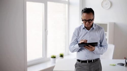 Mature asian businessman browsing online with tablet computer in modern office