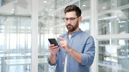 Businessman is using browsing mobile phone standing at workplace in a modern business office.