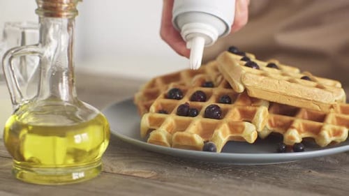 Waffles with Blueberries Being Decorated with Whipped Cream