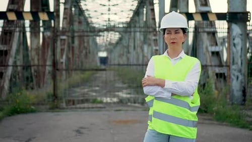 Female Engineer Stands Near an Old Metal Bridge