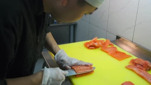 Side view asian sushi chef in white gloves slices fresh salmon fish fillet at sushi bar