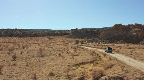 Aerial following car through desert landscape on remote dirt road, 4K