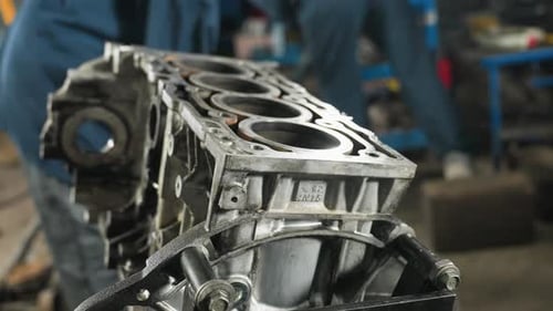 CloseUp of Car Engine in Workshop with Mechanics in Background