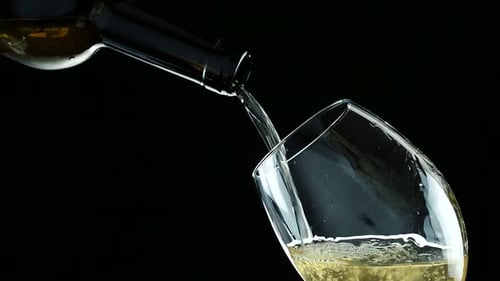 Pouring white wine into a glass, black background