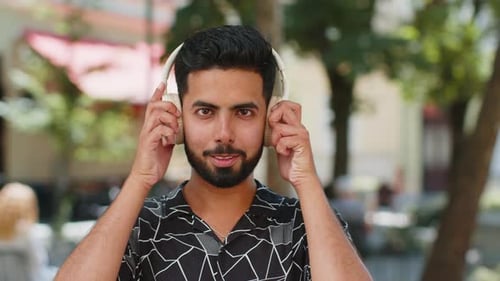 Man Putting on Headphones and Smiling in City