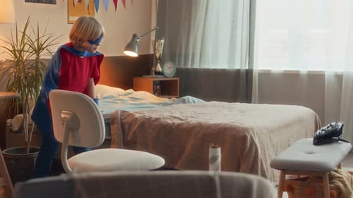Energetic Child Dressed as Superhero Plays in Bedroom