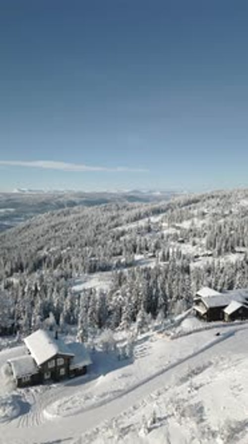 Vue aérienne hivernale d'un village de chalets nordiques à flanc de montagne enneigé en plein soleil