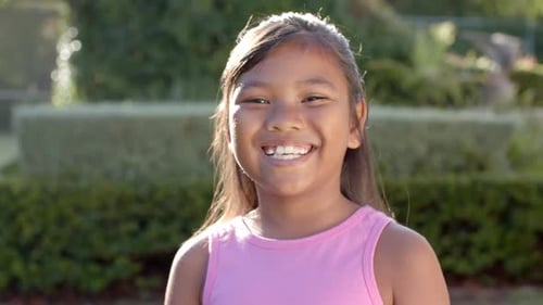 Menina sorridente em camiseta rosa curtindo ao ar livre, mostrando felicidade e alegria
