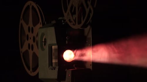 Close-up of a retro 16mm projector playing in the dark with volumetric light beaming from the bulb.