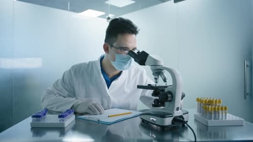 Männlicher Wissenschaftler schaut im modernen medizinischen Forschungslabor unter die Lupe