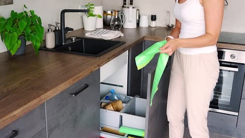 Mujer joven reemplaza la bolsa de basura en el basurero de la cocina, plástico, papel biológico y residuos mixtos