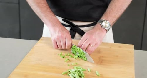 männlicher Koch schneidet mit seinem Messer auf dem Schneidebrett in seiner Küche präzise die grüne Bohne