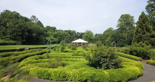 Low altitude flying over symmetrical green park towards white gazebo