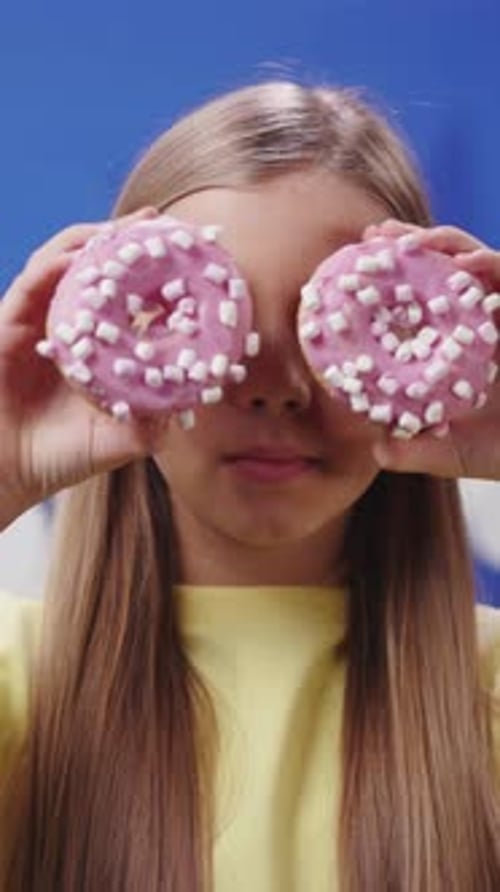 A Young Girl Joyfully and Playfully Holds a Delightful Assortment of Donuts with Pink Frosting