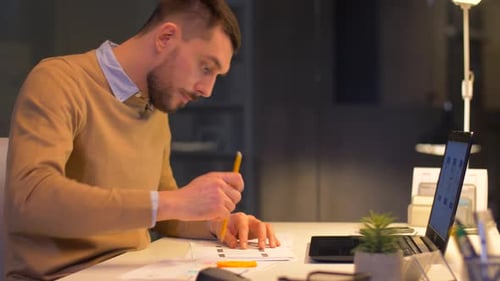 Man Working Late at Desk with Laptop and Phone