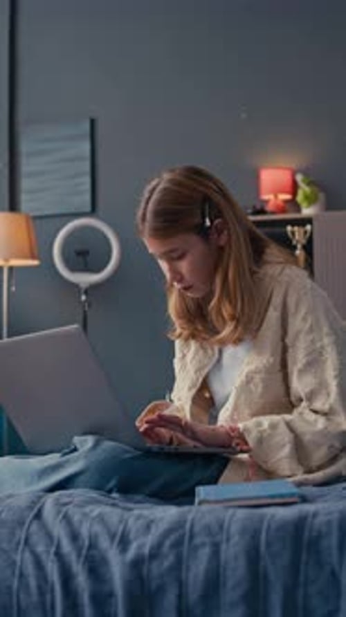 Teen Girl Using Laptop Sitting on Bed at Home
