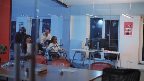 Colegas multiculturales montados en sillas para la destilación en una oficina de vidrio moderna, jóvenes felices