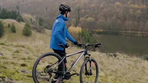 Cyclist Standing with Mountain Bike on Hillside