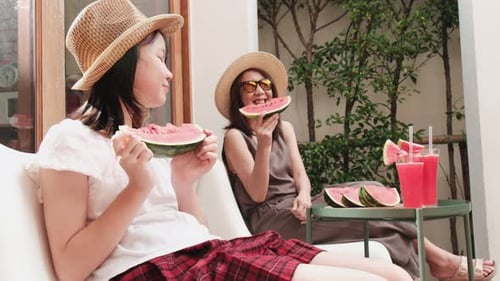 Girl and woman eating watermelon on a couch