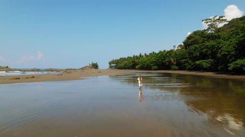 Woman in white dress walking alone on wide tropical beach in Costa Rica