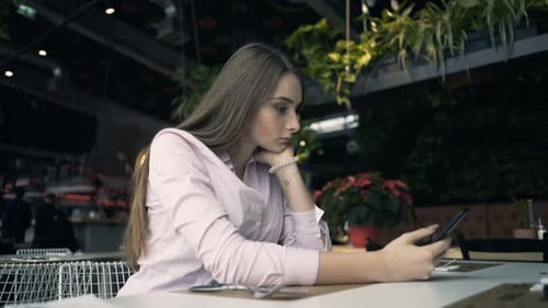 Pretty, Young Woman Texting on Smartphone Sitting in Cafe 20s