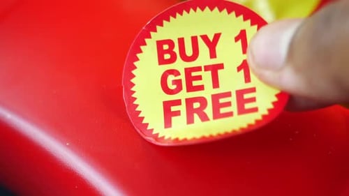 Hand Applies a Buy One Get One Free Sticker