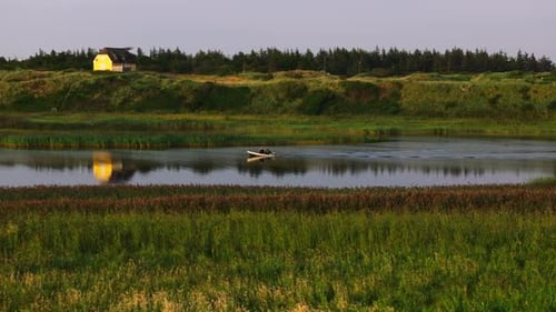 Fisherman Takes His Boat on the Calm Water of a River in Denmark As the Sun Sets and Casts a Warm