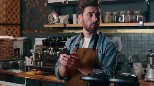 Confused Caucasian Barista Man Holding Mobile Phone Shrug Shoulders in Cafeteria Guy Waiter Unsure