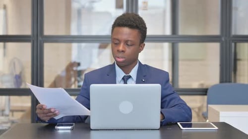 Young Adult Reviews Documents at Office Desk