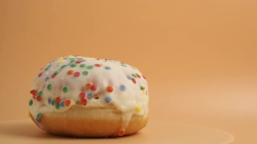 A donut covered with sugar glaze with multi-colored crumbs rotates on an orange background.