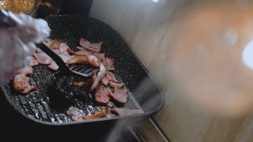 The Cook Stirs the Frying Bacon with a Spoon Camera Follows Cooking Bacon on Grill