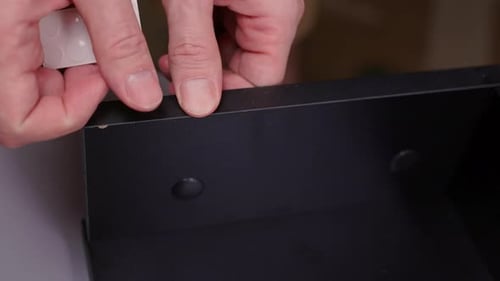 Pessoa aplicando adesivos autoadesivos transparentes com tampa de rosca em orifícios de parafusos de móveis pretos